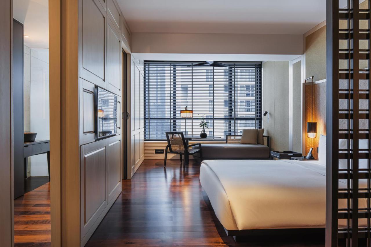 The Ruma Hotel And Residences Kuala Lumpur Eksteriør billede The photo shows a modern hotel room with a clean and minimalist design. The room features a large bed with white bedding positioned against a wall. There is a wooden floor that adds warmth to the space. A sitting area is visible in the background, fe