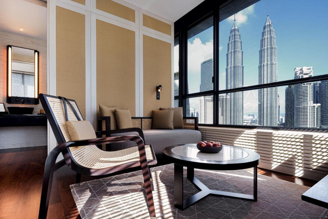The Ruma Hotel And Residences Kuala Lumpur Eksteriør billede The photo depicts a stylish and modern interior of a living space, featuring a seating area with a comfortable chair and a sofa. There's a round coffee table in the center, adorned with decorative items. The room has large windows that offer an impre